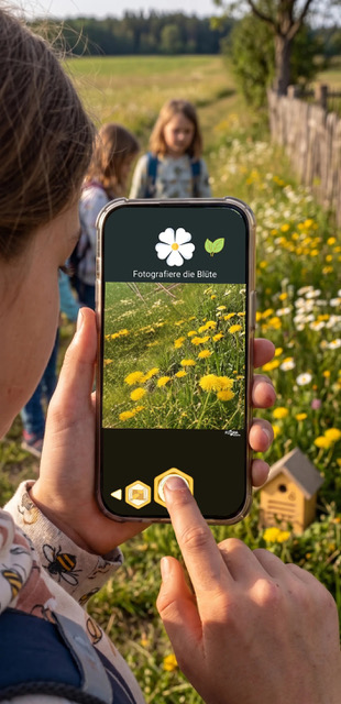 Kind mit Smartphone in der Hand, dass Blumen fotografiert.